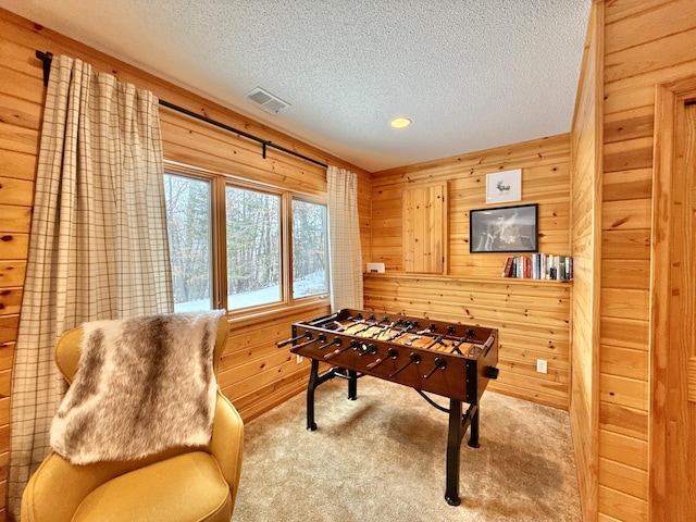 game room with carpet, visible vents, wood walls, and a textured ceiling