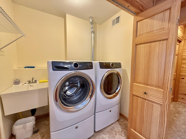 laundry area with a textured ceiling, laundry area, a sink, visible vents, and washing machine and clothes dryer