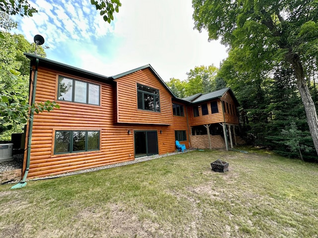 back of property featuring an outdoor fire pit, log veneer siding, a lawn, and central AC