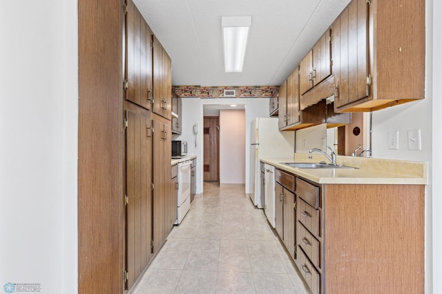 kitchen featuring light tile patterned floors, light countertops, brown cabinetry, a sink, and white appliances