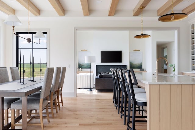 dining space with baseboards, beamed ceiling, and light wood finished floors