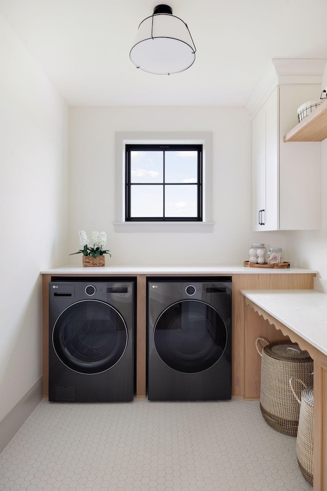 clothes washing area with washing machine and dryer, cabinet space, and baseboards