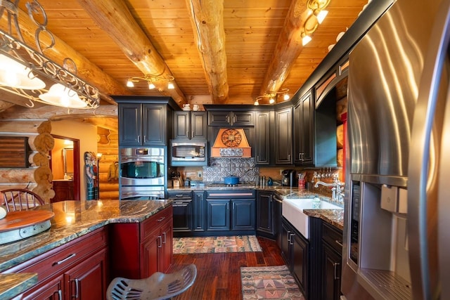 kitchen with dark wood-type flooring, dark stone counters, stainless steel appliances, and a sink