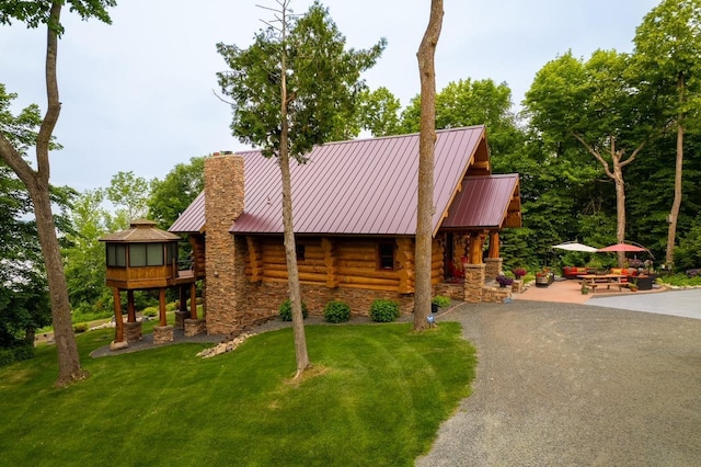 exterior space featuring a chimney, log siding, aphalt driveway, a standing seam roof, and a front lawn