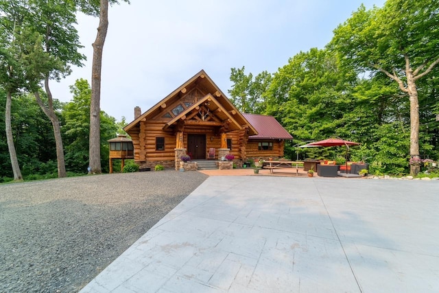 cabin with log exterior, a chimney, a patio area, and an outdoor living space