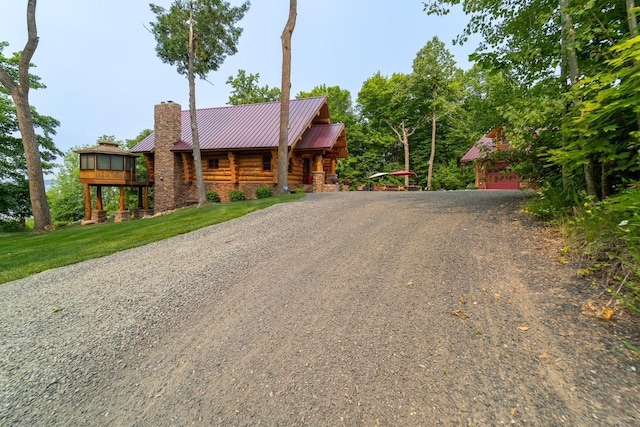 cabin featuring metal roof, a front yard, log exterior, a chimney, and gravel driveway