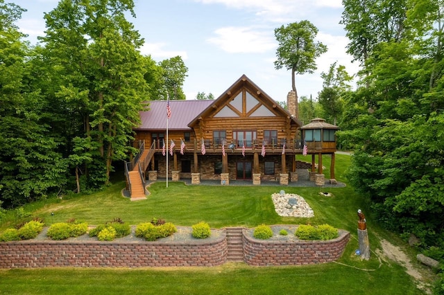 rear view of property with a deck, metal roof, stairs, stone siding, and a lawn