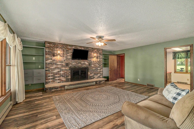 living room with a textured ceiling, a baseboard heating unit, visible vents, a brick fireplace, and dark wood-style floors