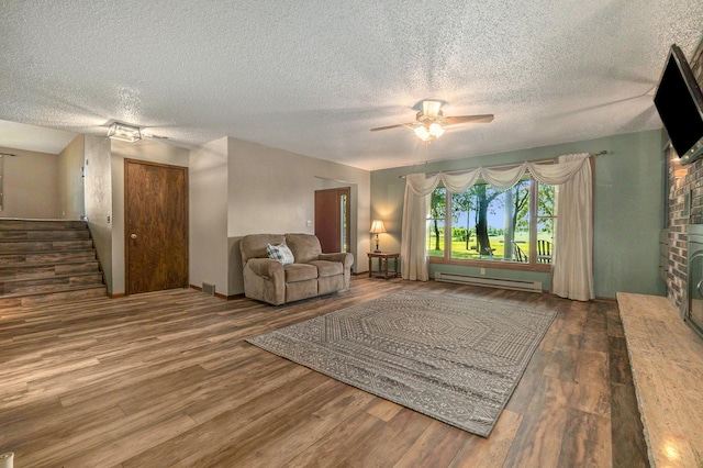 unfurnished living room featuring ceiling fan, wood finished floors, stairway, baseboard heating, and a brick fireplace