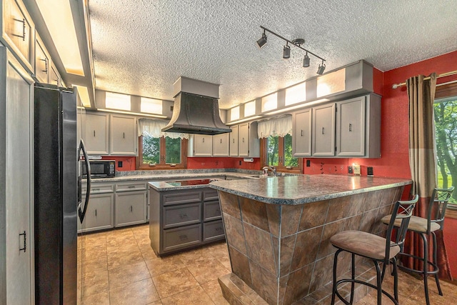 kitchen featuring black microwave, a breakfast bar area, freestanding refrigerator, a center island, and island exhaust hood