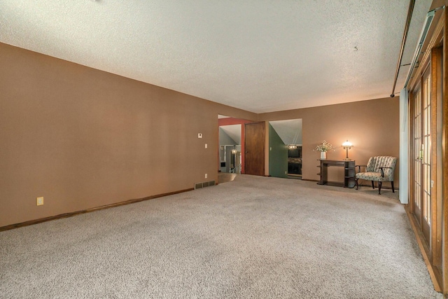 empty room with carpet floors, visible vents, a textured ceiling, and baseboards