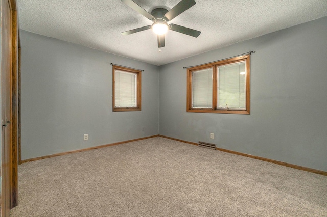 empty room with baseboards, visible vents, a textured ceiling, and light colored carpet