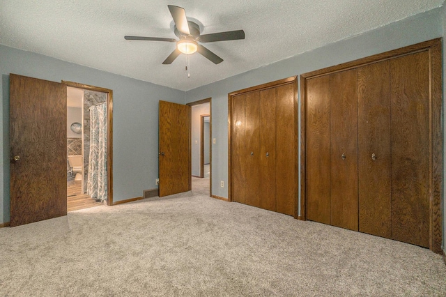 unfurnished bedroom with multiple closets, light carpet, ceiling fan, a textured ceiling, and ensuite bath