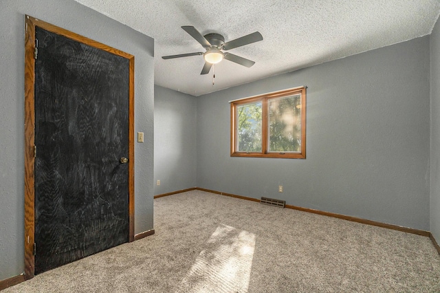 empty room with a textured ceiling, carpet flooring, visible vents, baseboards, and a ceiling fan