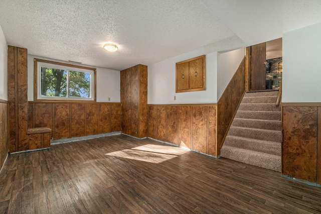 empty room featuring dark wood-style flooring, stairway, wainscoting, wood walls, and a textured ceiling