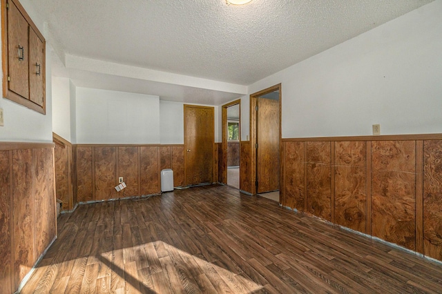 spare room featuring a wainscoted wall, dark wood-style flooring, a textured ceiling, and wood walls