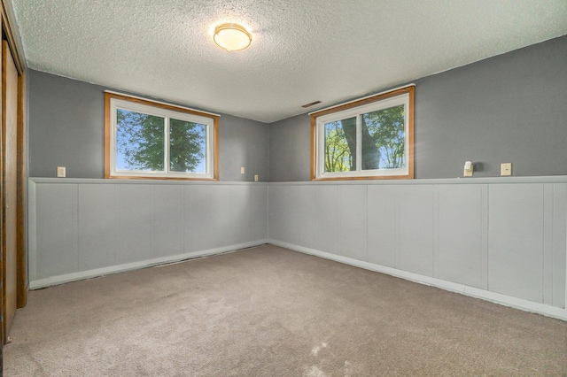 carpeted spare room featuring a textured ceiling, wainscoting, plenty of natural light, and visible vents