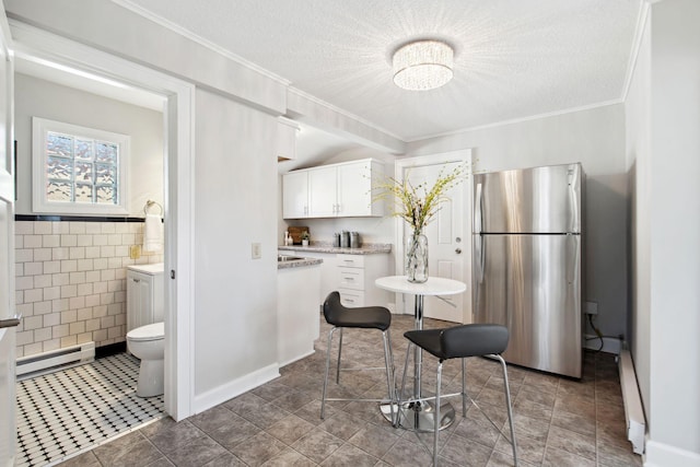 kitchen with freestanding refrigerator, light countertops, a textured ceiling, a baseboard heating unit, and white cabinetry