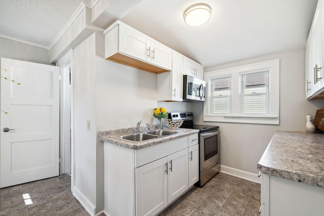 kitchen featuring baseboards, white cabinets, stainless steel appliances, crown molding, and a sink