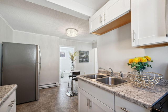 kitchen featuring freestanding refrigerator, white cabinets, a sink, and baseboard heating