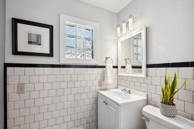 bathroom with a wealth of natural light, vanity, toilet, and tile walls