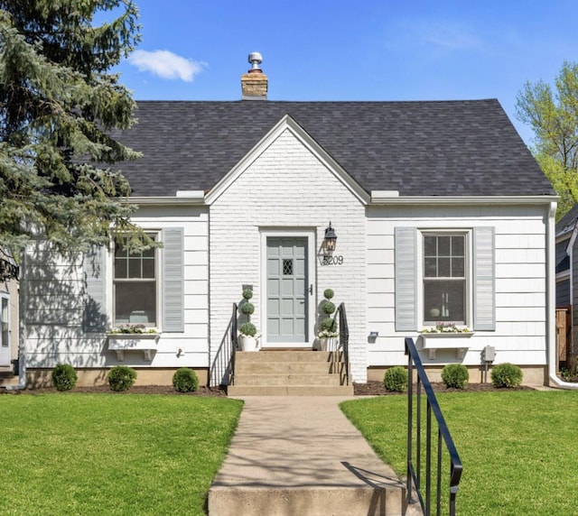 view of front of property with roof with shingles, a front lawn, a chimney, and brick siding