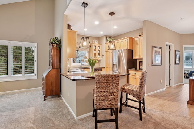 kitchen featuring light brown cabinets, light colored carpet, a peninsula, baseboards, and stainless steel fridge