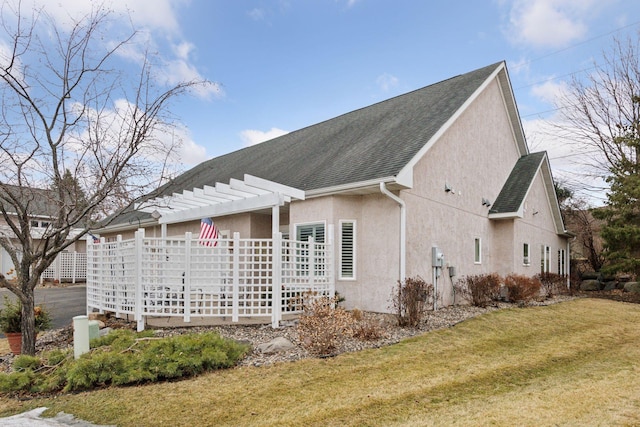 view of side of property featuring a shingled roof, stucco siding, a lawn, and a pergola