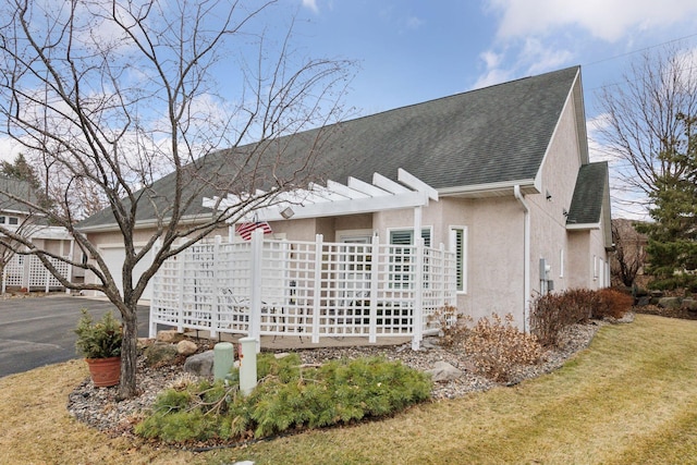 view of side of home featuring roof with shingles, a pergola, a lawn, and stucco siding