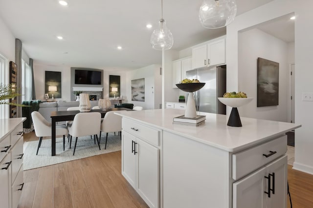 kitchen featuring a center island, light wood finished floors, light countertops, freestanding refrigerator, and white cabinets