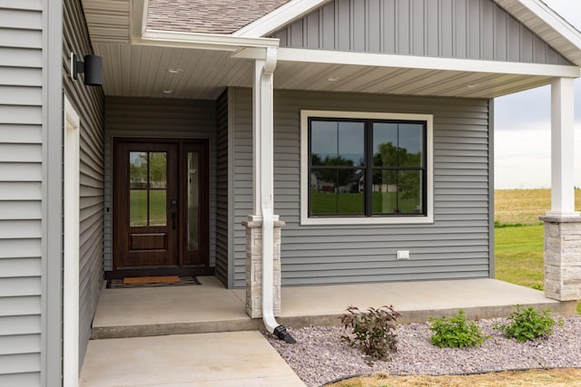 property entrance with covered porch, a shingled roof, and board and batten siding