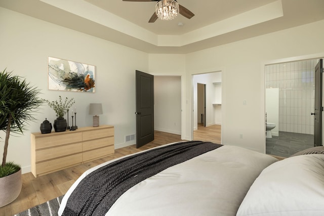 bedroom featuring a raised ceiling, wood finished floors, visible vents, and connected bathroom