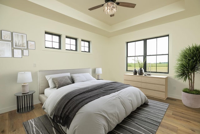 bedroom featuring a tray ceiling, multiple windows, wood finished floors, and baseboards