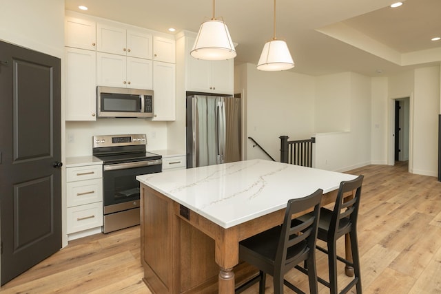 kitchen with white cabinets, a kitchen island, appliances with stainless steel finishes, decorative light fixtures, and light wood-style floors