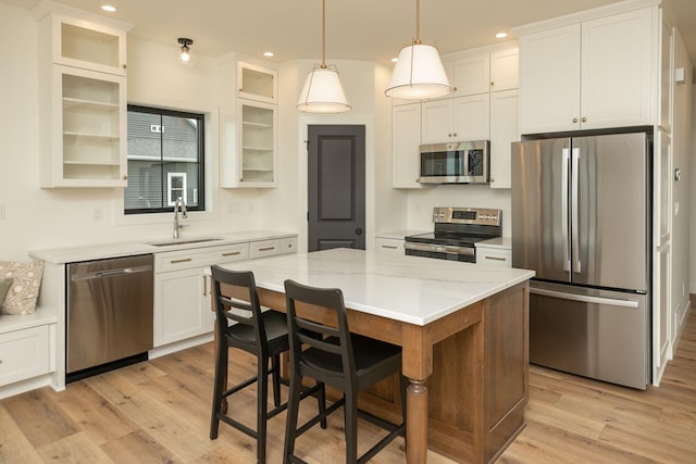 kitchen featuring white cabinets, a kitchen island, appliances with stainless steel finishes, glass insert cabinets, and a sink