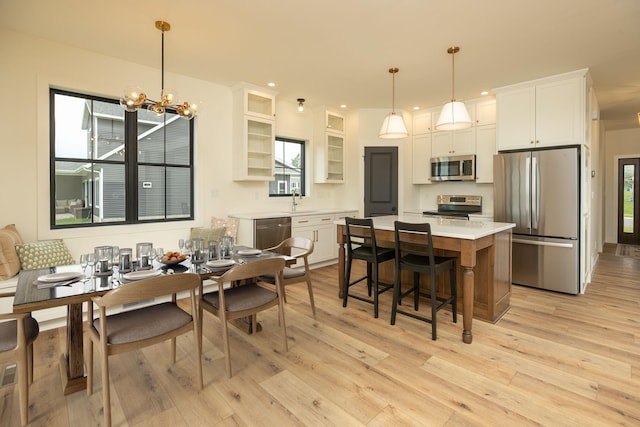 kitchen featuring white cabinets, a center island, decorative light fixtures, stainless steel appliances, and light countertops