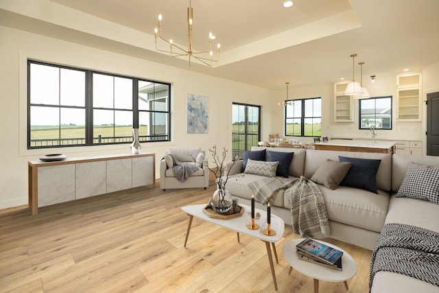 living area with baseboards, a raised ceiling, light wood-style floors, a chandelier, and recessed lighting