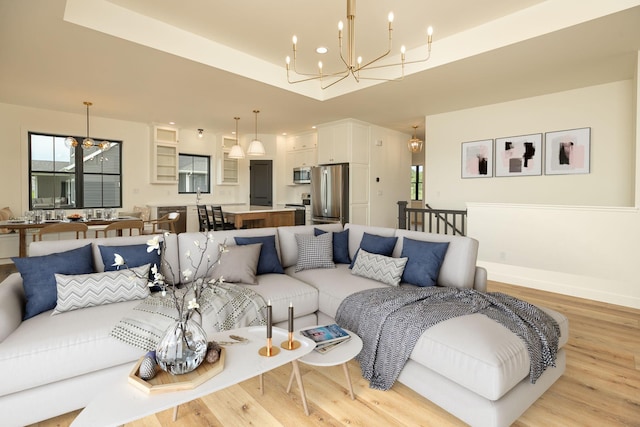 living area with baseboards, a tray ceiling, light wood-style flooring, and an inviting chandelier