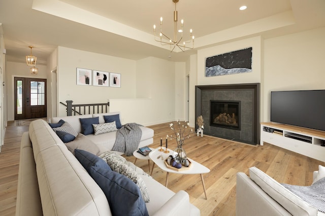 living room featuring a chandelier, recessed lighting, a fireplace, a tray ceiling, and light wood finished floors