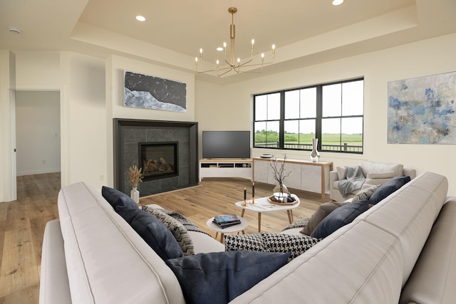 living room featuring a tiled fireplace, wood finished floors, a tray ceiling, a chandelier, and recessed lighting