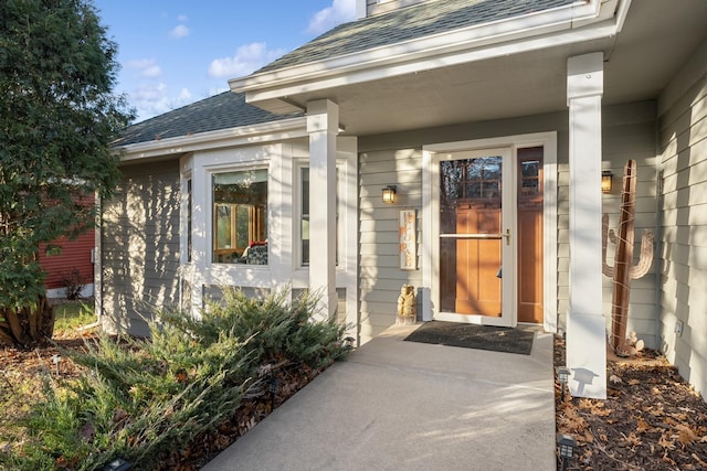 doorway to property featuring covered porch and roof with shingles