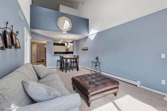 living room featuring a baseboard heating unit, a high ceiling, baseboards, carpet, and an inviting chandelier