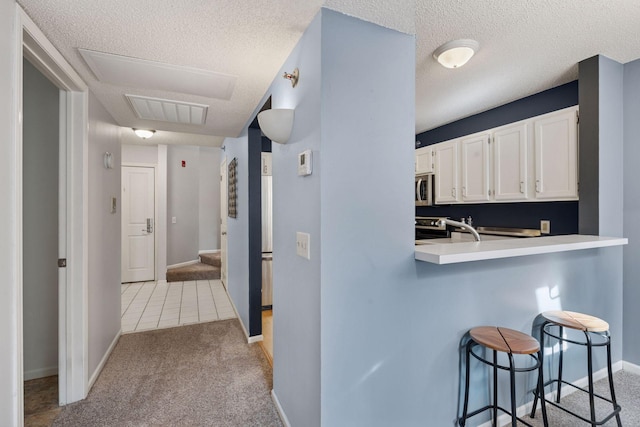 kitchen with carpet floors, stainless steel appliances, light countertops, white cabinets, and a kitchen breakfast bar