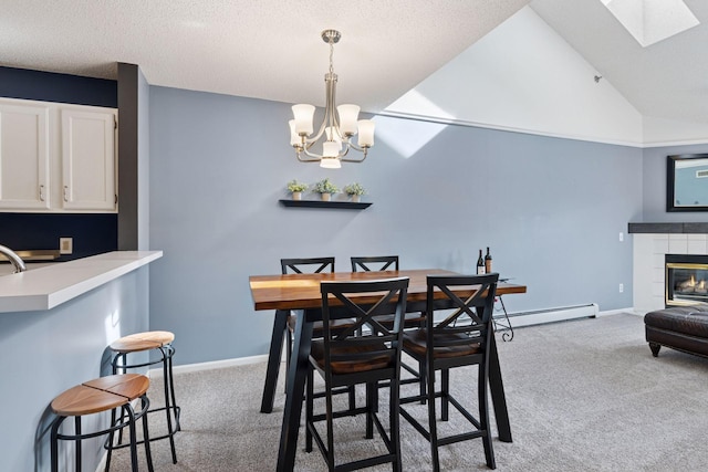 carpeted dining space with a notable chandelier, a baseboard heating unit, a tile fireplace, vaulted ceiling with skylight, and baseboards