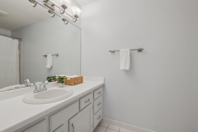 full bath with a textured ceiling, tile patterned flooring, vanity, and baseboards