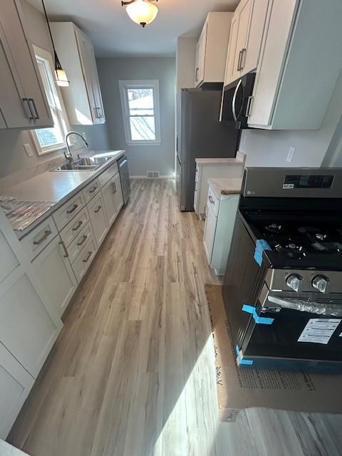 kitchen featuring light countertops, light wood-style floors, white cabinets, stainless steel appliances, and a sink