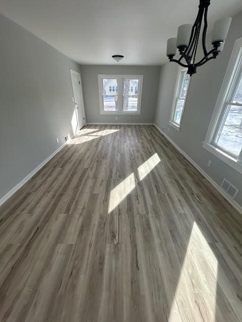 unfurnished living room featuring visible vents, wood finished floors, baseboards, and a chandelier