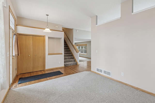 carpeted entryway with visible vents, stairs, baseboards, and wood finished floors