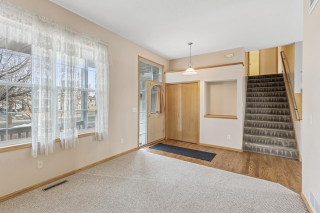 carpeted entryway featuring a wealth of natural light, visible vents, stairs, and baseboards