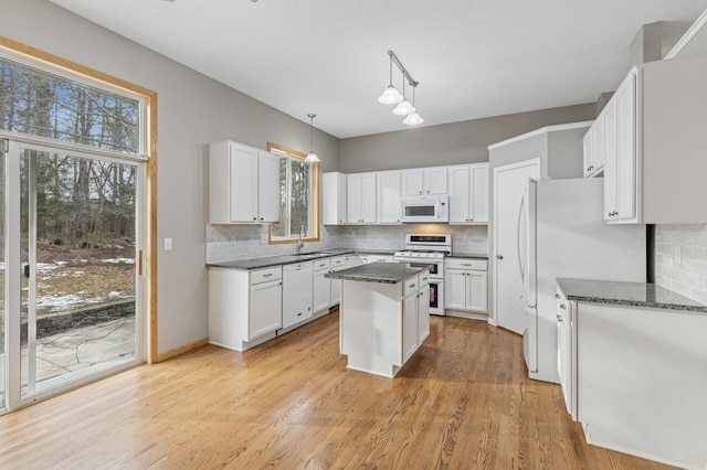 kitchen with a sink, white appliances, white cabinets, and a center island